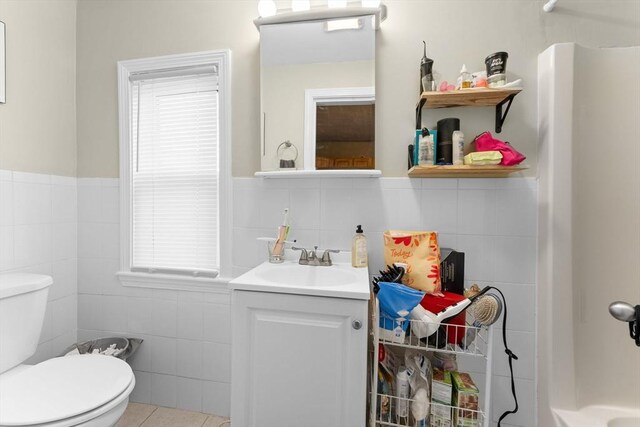 full bath featuring wainscoting, vanity, tile walls, walk in shower, and toilet