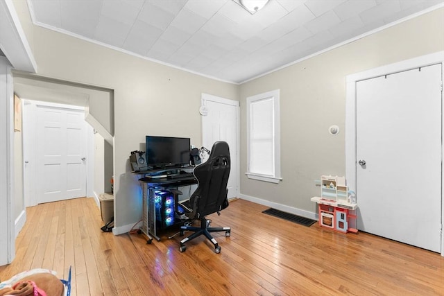 office area with light wood-type flooring, baseboards, visible vents, and crown molding