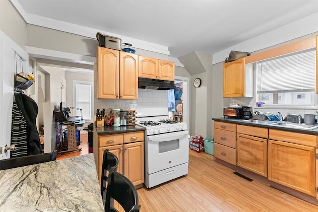 kitchen featuring light wood finished floors, a sink, tasteful backsplash, white range with gas stovetop, and under cabinet range hood