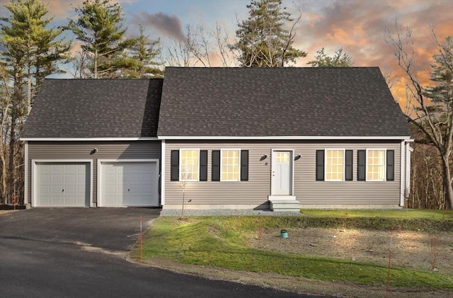 cape cod-style house featuring entry steps, an attached garage, driveway, and a shingled roof