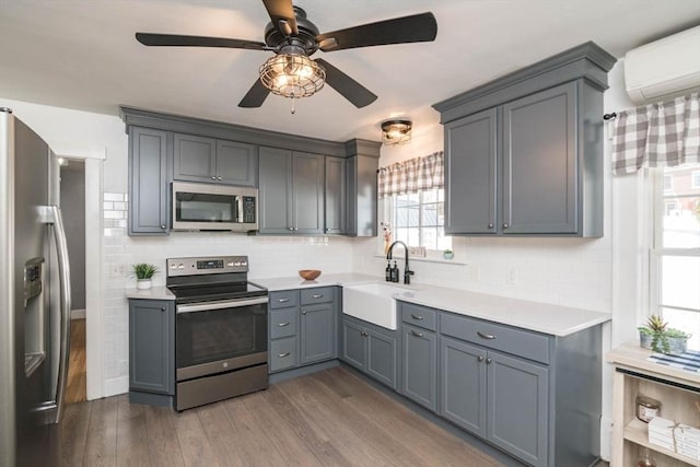 kitchen with wood finished floors, stainless steel appliances, a sink, and an AC wall unit