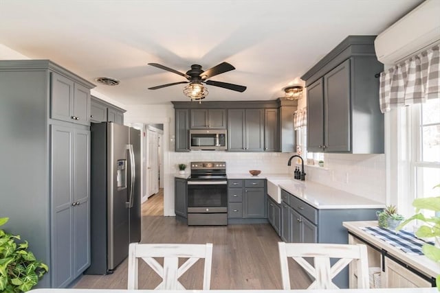 kitchen with a wall unit AC, gray cabinetry, stainless steel appliances, a sink, and visible vents