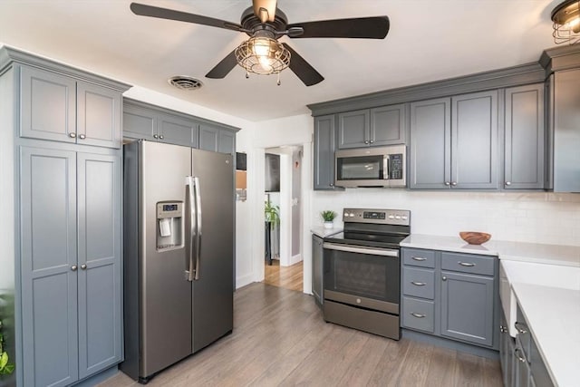 kitchen featuring stainless steel appliances, tasteful backsplash, light countertops, visible vents, and light wood-style floors