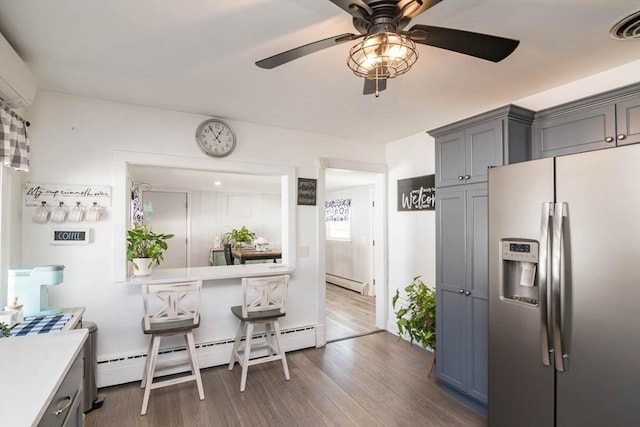 kitchen featuring gray cabinetry, a baseboard heating unit, wood finished floors, visible vents, and stainless steel fridge