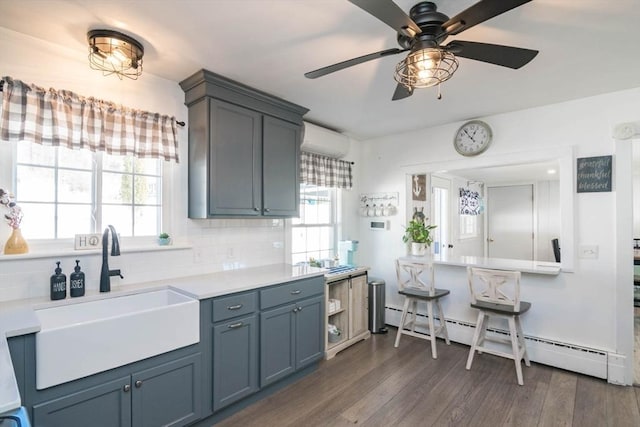 kitchen with dark wood-style floors, a sink, an AC wall unit, a baseboard heating unit, and backsplash