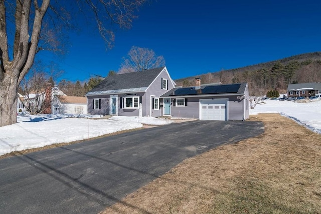 view of front of house featuring an attached garage, driveway, a chimney, and solar panels