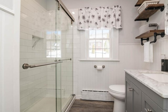 bathroom with toilet, wood finished floors, baseboard heating, wainscoting, and a stall shower