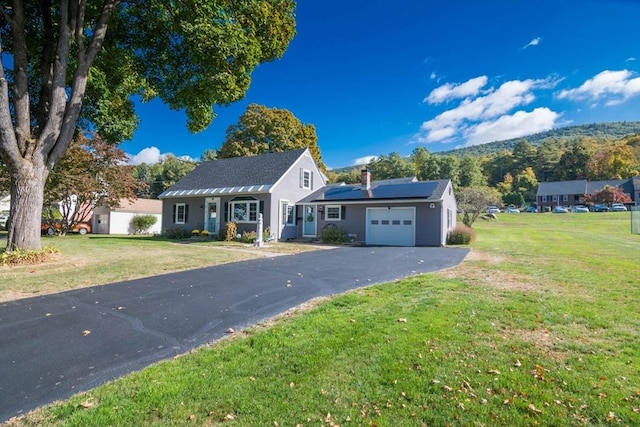 ranch-style house featuring a garage, a chimney, aphalt driveway, roof mounted solar panels, and a front yard