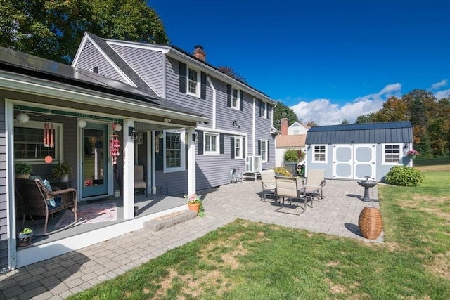 back of property featuring an outdoor structure, a yard, roof mounted solar panels, a storage unit, and a chimney