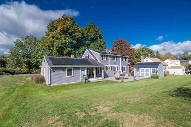 rear view of property featuring a yard, a patio, an outdoor structure, and solar panels