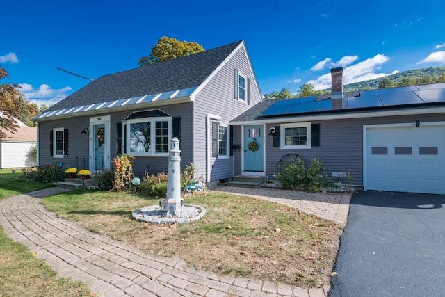 view of front of property with roof mounted solar panels, driveway, a chimney, and an attached garage