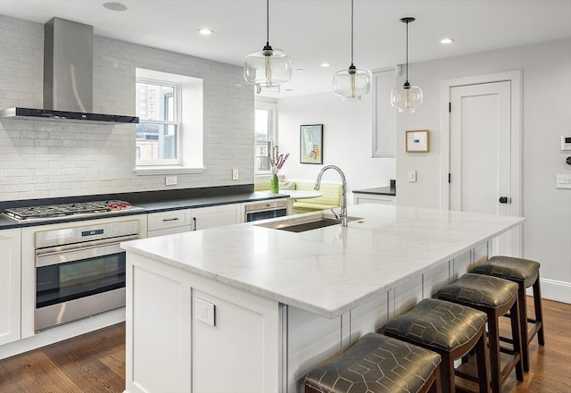 kitchen with wall chimney range hood, appliances with stainless steel finishes, dark wood finished floors, a sink, and white cabinetry