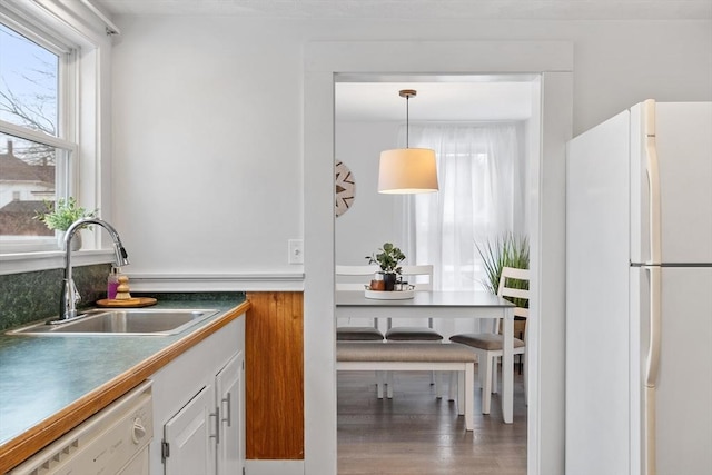 kitchen with white appliances, white cabinets, dark countertops, pendant lighting, and a sink