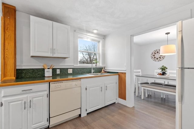 kitchen with white appliances, a sink, white cabinetry, hanging light fixtures, and light wood finished floors