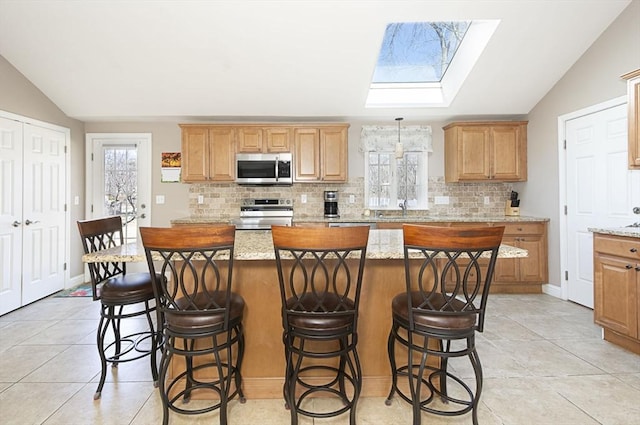 kitchen featuring decorative backsplash, vaulted ceiling with skylight, a center island, and stainless steel appliances