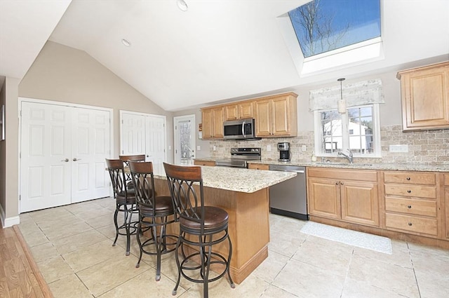 kitchen with light stone countertops, lofted ceiling with skylight, a breakfast bar area, decorative backsplash, and stainless steel appliances