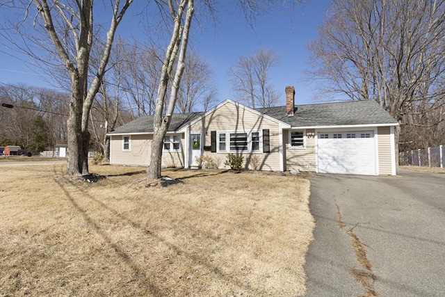 ranch-style home featuring a front yard, roof with shingles, a chimney, a garage, and aphalt driveway