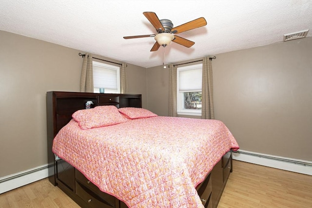 bedroom with a baseboard heating unit, a textured ceiling, visible vents, and light wood-style flooring