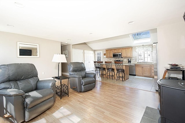 living area with lofted ceiling with skylight, light wood-style floors, and baseboards