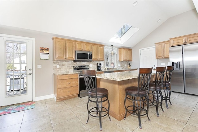 kitchen featuring a skylight, stainless steel appliances, a kitchen bar, backsplash, and a center island