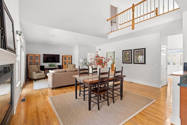 dining space featuring visible vents, a high end fireplace, baseboards, a high ceiling, and light wood-style flooring