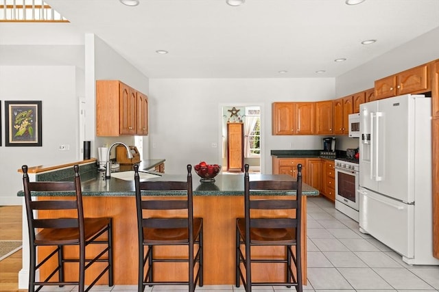 kitchen featuring white appliances, a peninsula, dark countertops, and a sink