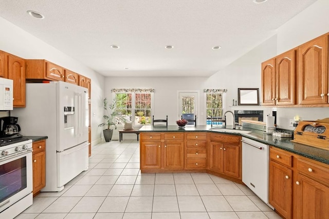kitchen featuring a sink, dark countertops, a peninsula, and white appliances