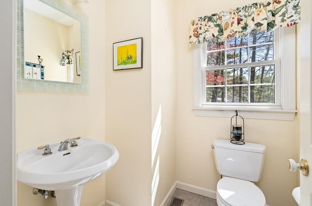 half bath with visible vents, toilet, baseboards, tile patterned floors, and a sink