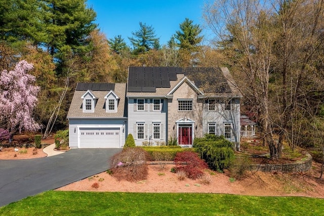 colonial house with a garage, roof mounted solar panels, and driveway