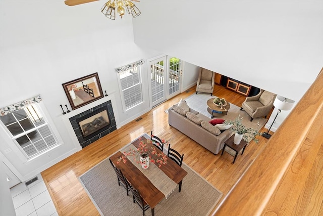 living area with visible vents, a fireplace, wood finished floors, baseboards, and a high ceiling