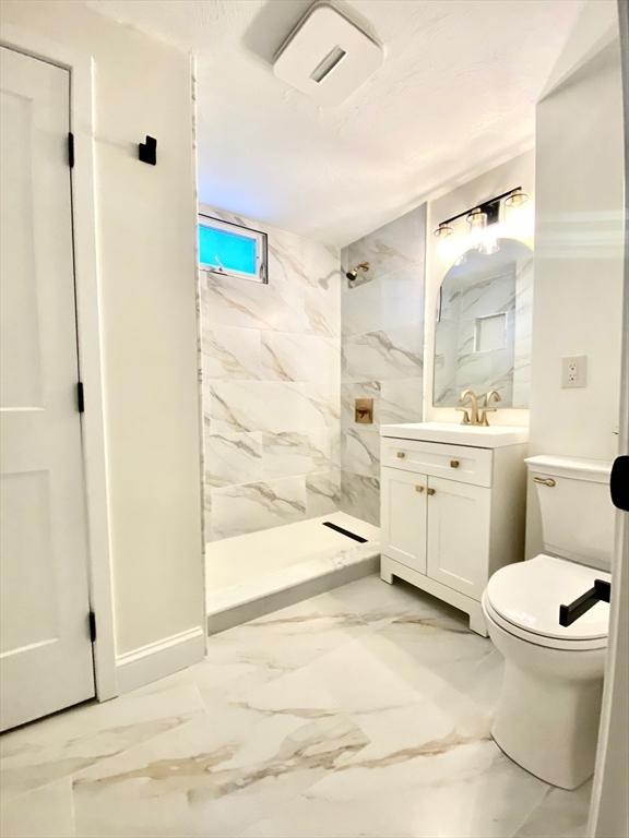 bathroom featuring vanity, tiled shower, and toilet