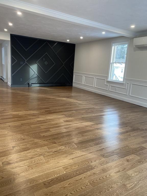 unfurnished room featuring ornamental molding, hardwood / wood-style floors, and a wall mounted AC