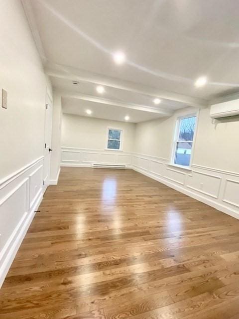 unfurnished room featuring beamed ceiling, wood-type flooring, a baseboard heating unit, and a wall mounted air conditioner