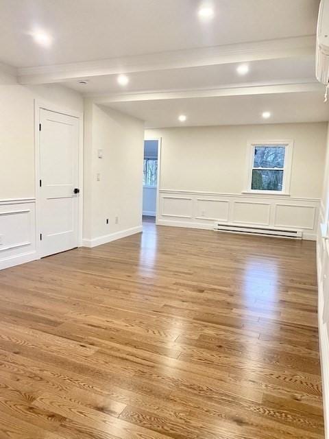 empty room featuring hardwood / wood-style flooring, a baseboard radiator, and beam ceiling