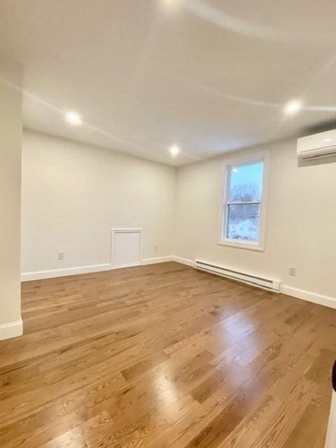 basement featuring wood-type flooring, a wall unit AC, and a baseboard heating unit