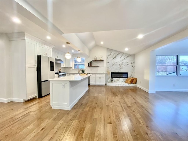 kitchen featuring lofted ceiling, pendant lighting, white cabinetry, stainless steel appliances, and a kitchen island