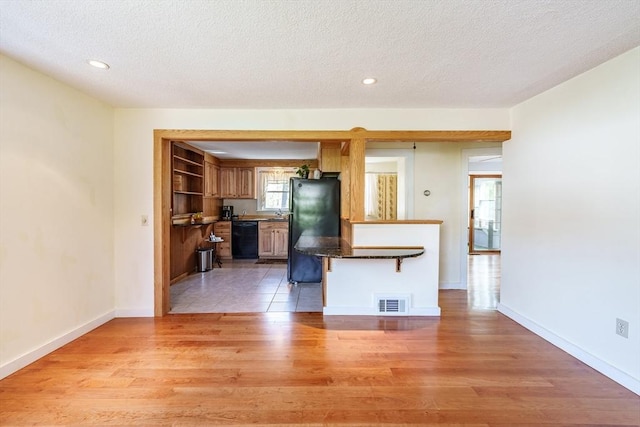 kitchen featuring visible vents, a textured ceiling, light wood finished floors, and black appliances