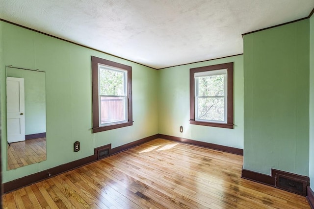 empty room featuring light wood-style floors, plenty of natural light, and visible vents