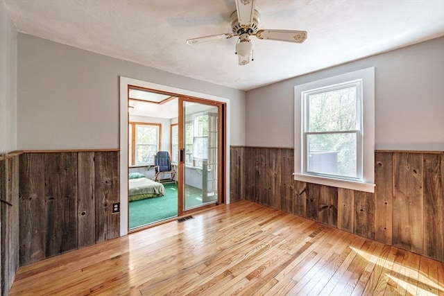 empty room featuring wood-type flooring, wood walls, visible vents, a wainscoted wall, and a ceiling fan