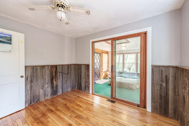 empty room featuring visible vents, wood walls, wainscoting, and wood finished floors