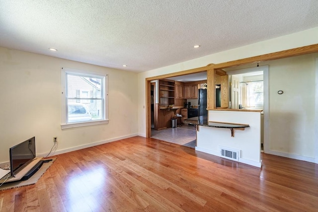 unfurnished living room featuring a textured ceiling, visible vents, a healthy amount of sunlight, and light wood-type flooring