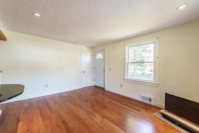 unfurnished living room with visible vents, a textured ceiling, baseboards, and hardwood / wood-style floors