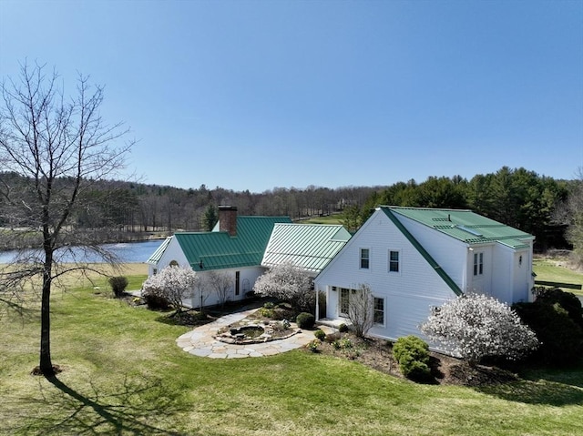 view of side of home with a chimney, a view of trees, metal roof, and a lawn