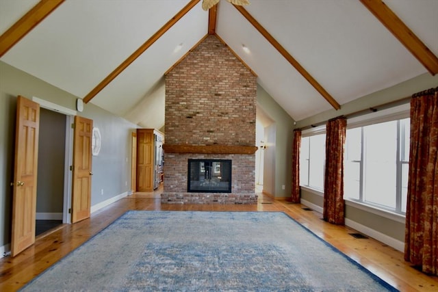unfurnished living room featuring beam ceiling, hardwood / wood-style flooring, a brick fireplace, and baseboards
