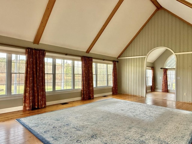 unfurnished living room featuring visible vents, arched walkways, a wealth of natural light, and high vaulted ceiling