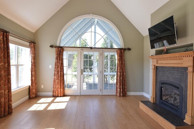 unfurnished living room with high vaulted ceiling, baseboards, light wood-style flooring, and a fireplace