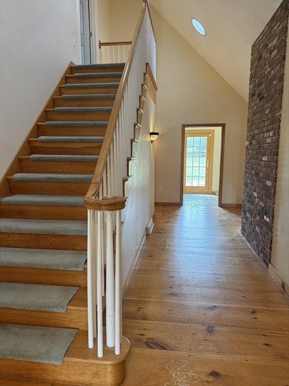 staircase featuring wood-type flooring, recessed lighting, high vaulted ceiling, and baseboards