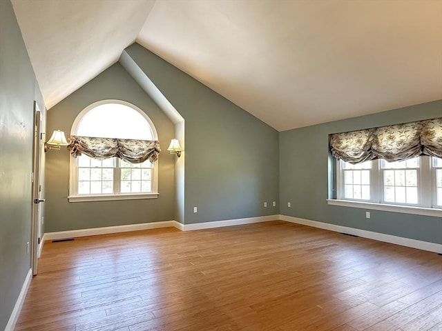 unfurnished room featuring hardwood / wood-style floors, visible vents, baseboards, and vaulted ceiling