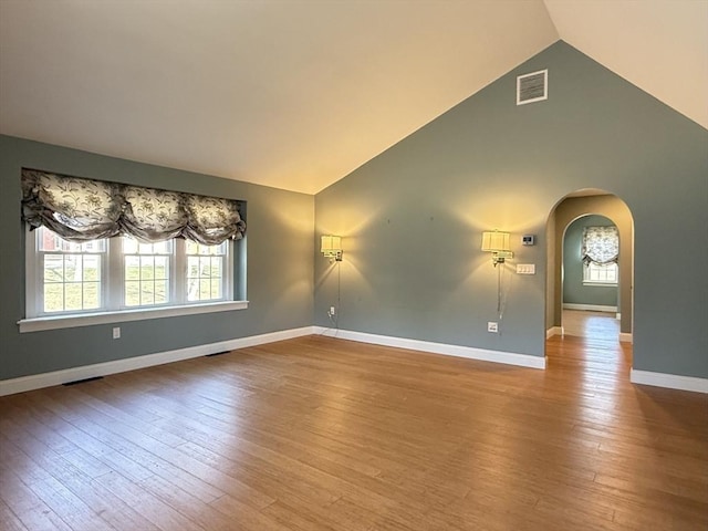 spare room with visible vents, vaulted ceiling, baseboards, arched walkways, and hardwood / wood-style floors