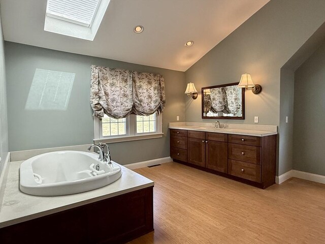 full bath featuring lofted ceiling with skylight, wood finished floors, vanity, and baseboards